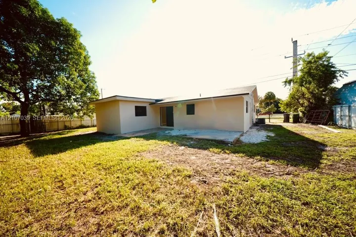 Exterior rear view featuring a stucco facade, concrete patio, and mature trees