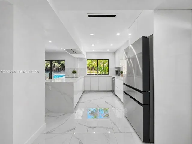 Modern kitchen featuring high-gloss cabinetry, waterfall edge stone countertops, large-format polished flooring, stainless steel appliances, and recessed lighting