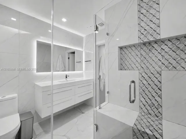 Modern floating vanity with a seamless countertop, integrated basin, and back-lit mirror, complemented by a walk-in glass-enclosed shower featuring detailed stone-tile inlay and a built-in bench