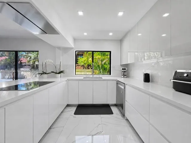 Modern kitchen featuring high-gloss cabinetry, solid surface countertops, a stainless steel range hood, stone-finish tile flooring, and integrated stainless steel appliances