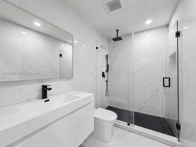 Modern bathroom featuring a wall-mounted vanity, large-format stone-look wall tile, walk-in glass shower enclosure, matte black rainfall shower system, and recessed wall niche