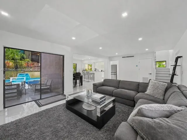 Open-concept living space featuring high-gloss tile flooring, recessed lighting, and large sliding glass doors providing outdoor access to the pool area