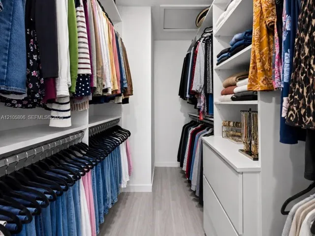 Walk-in closet featuring floor-to-ceiling white built-in shelving, custom cabinetry with integrated drawers, multi-level hanging rods, and wood-finish flooring