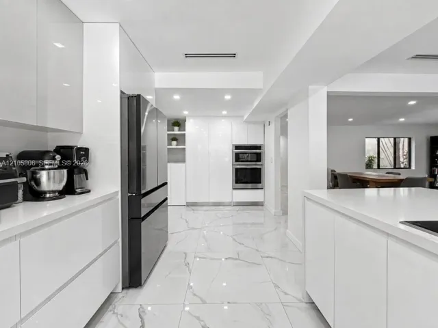 Modern kitchen featuring high-gloss cabinetry, white solid-surface countertops, large-format tile flooring with veining, and stainless steel built-in double wall ovens