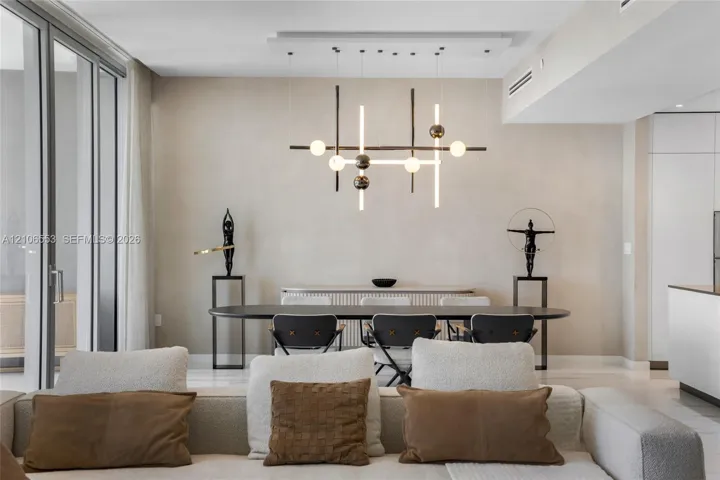 Modern chandelier with structural metallic frame and spherical lighting elements, floor-to-ceiling glass panel door, light-toned wall finishes, and polished flooring