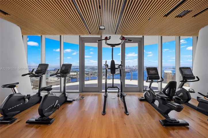 Floor-to-ceiling glass walls, linear wood slat ceiling, wood-finish flooring, and dual glass-paneled entry doors