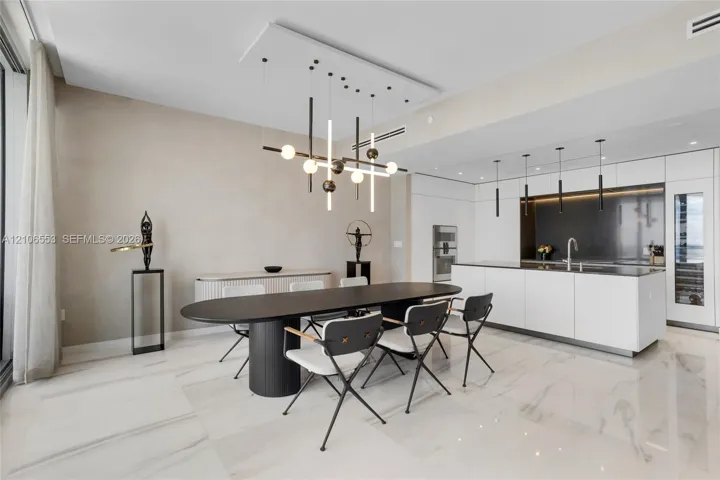 Open-concept interior featuring large-format stone flooring, a center island with integrated sink, built-in panel-ready appliances, and a geometric chandelier with linear and spherical lighting elements