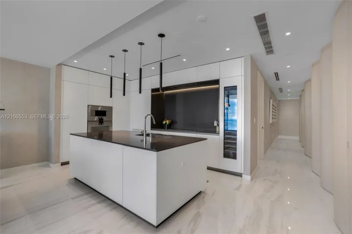 Modern kitchen featuring a central island with a stone-surface countertop, flat-panel cabinetry, integrated wine refrigeration, and matte black linear pendant lighting