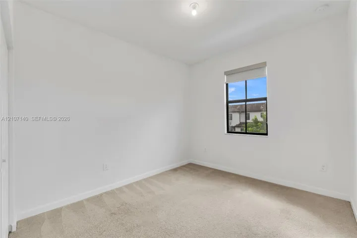 Neutral-toned wall paint, plush carpeting, and a single-hung window with a dark frame finish