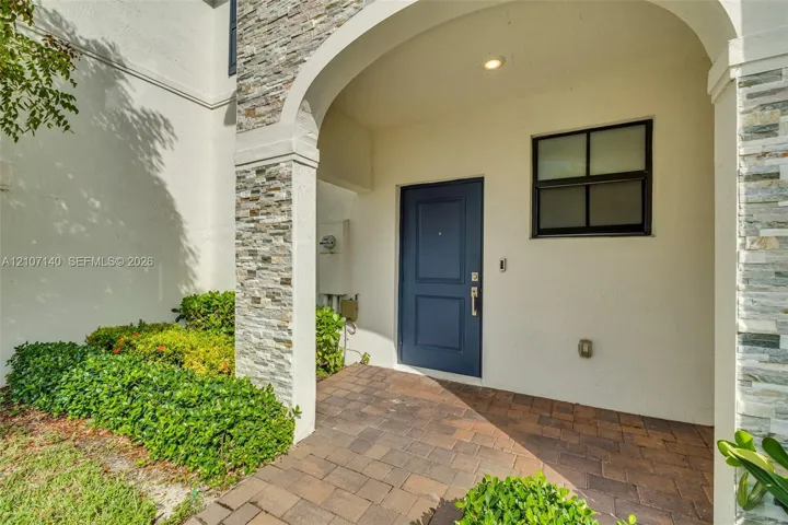 Covered entryway featuring a stone veneer accent pillar, a dark blue solid-panel door, and paved brick flooring
