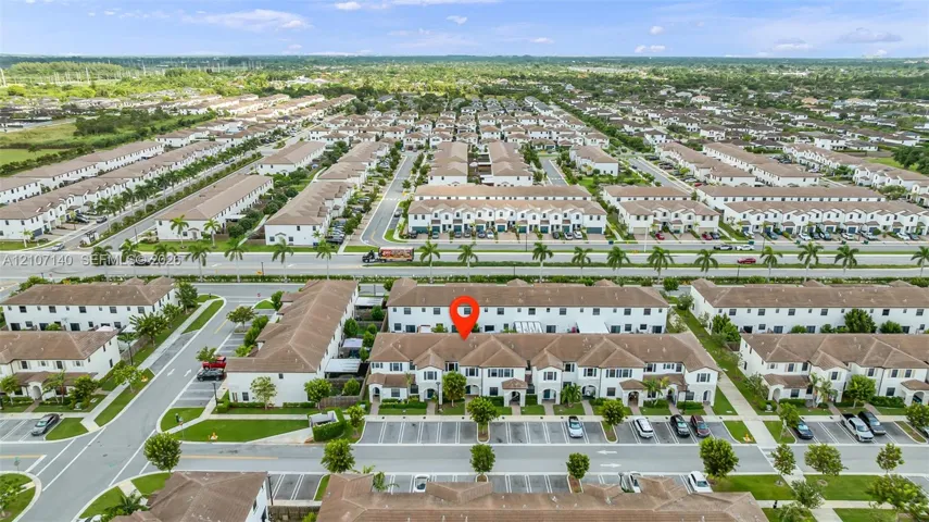 Aerial perspective of a multi-unit residential building featuring a light-toned stucco exterior, shingled roof lines, and dedicated surface parking