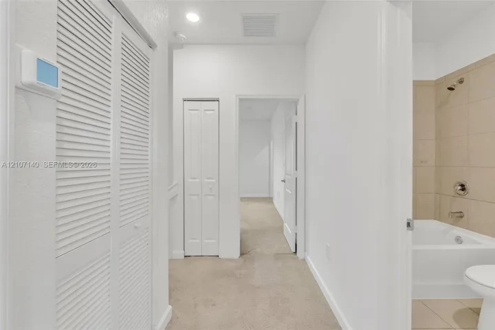 Hallway featuring dual bifold closets, neutral carpeting, recessed ceiling lighting, and a bathroom equipped with a porcelain tub, showerhead, and wall-mounted plumbing fixtures