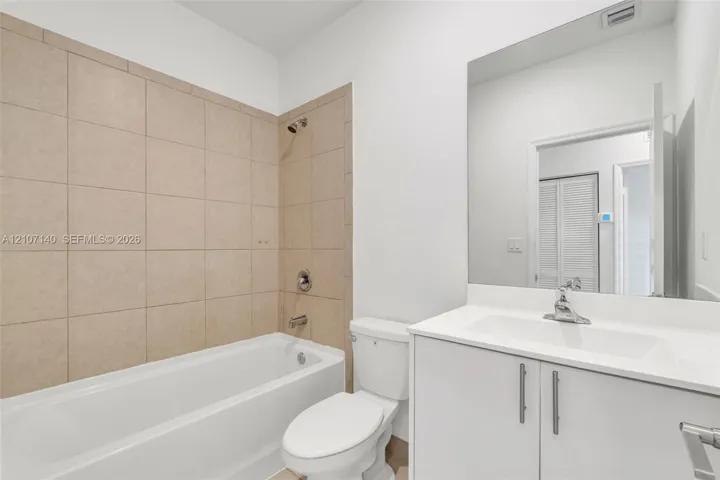 Bathroom featuring a white vanity cabinet with a solid-surface countertop, an integrated sink, full-width mirror, and a tub-shower combination with floor-to-ceiling neutral tile surround