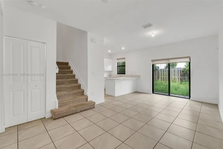 Open-concept floor plan with ceramic tile flooring, kitchen island, carpeted staircase, and sliding glass doors
