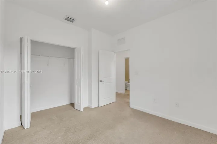 Neutral-toned interior space featuring beige carpeting, white walls, a multi-panel door, and a closet with bifold doors