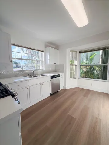 Kitchen featuring white shaker-style cabinetry, wood-finish flooring, stainless steel dishwasher, stone-finish backsplash, and a bay window