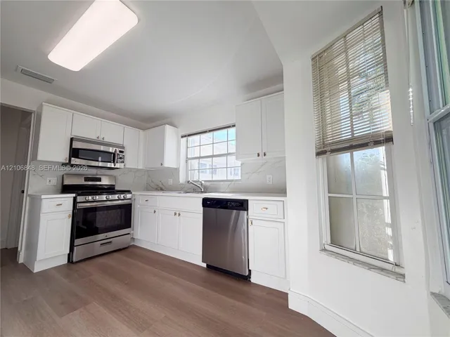 Kitchen featuring white shaker-style cabinetry, stone-patterned backsplash, stainless steel appliances, and wood-finish flooring
