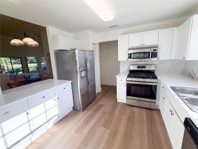 Kitchen featuring white shaker-style cabinetry, wood-finish flooring, stainless steel appliances, and solid surface countertops with a tiled backsplash