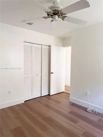 Wood-finish flooring, white louvered closet doors, and ceiling fan with integrated light fixture