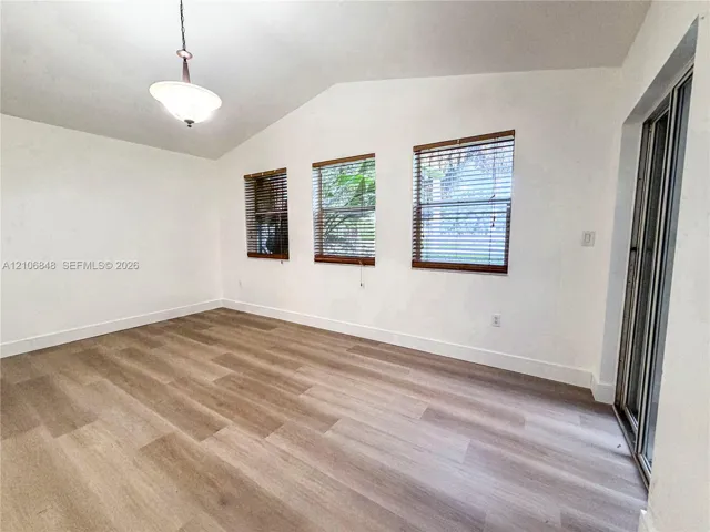 Vaulted ceilings, wood-finish flooring, three windows with horizontal blinds, and sliding glass door