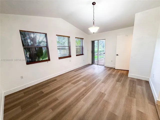 Room featuring vaulted ceilings, wood-finish flooring, three windows with horizontal blinds, a hanging pendant light fixture, and a sliding glass door