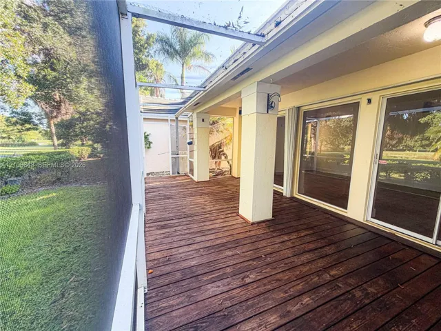 Screened-in porch featuring wood-finish decking, structural support pillars, and glass sliding door access
