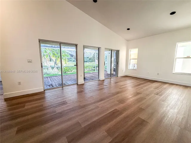 Vaulted ceilings, wood-finish flooring, recessed lighting, and multiple sliding glass doors providing outdoor access