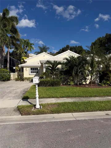 Single-story exterior featuring a light-toned stucco façade, dual-gabled roofline, paver driveway, and established palm landscaping