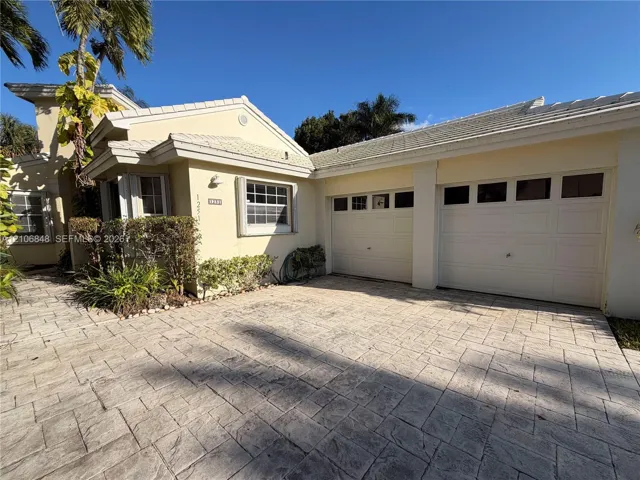 Stucco exterior with a tiled roof, paver driveway, and a two-car garage featuring paneled doors with window inserts