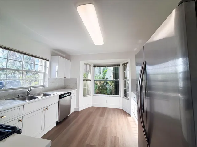 Kitchen featuring wood-finish flooring, white cabinetry, stainless steel appliances, a double-basin sink, and a bay window