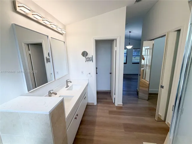 Double-sink vanity featuring a stone-surface countertop, wood-finish flooring, wall-mounted light fixtures, and dual framed mirrors