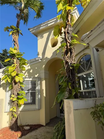 Stucco exterior featuring an arched entryway, decorative oculus window, arched window with muntin detailing, and mature palms