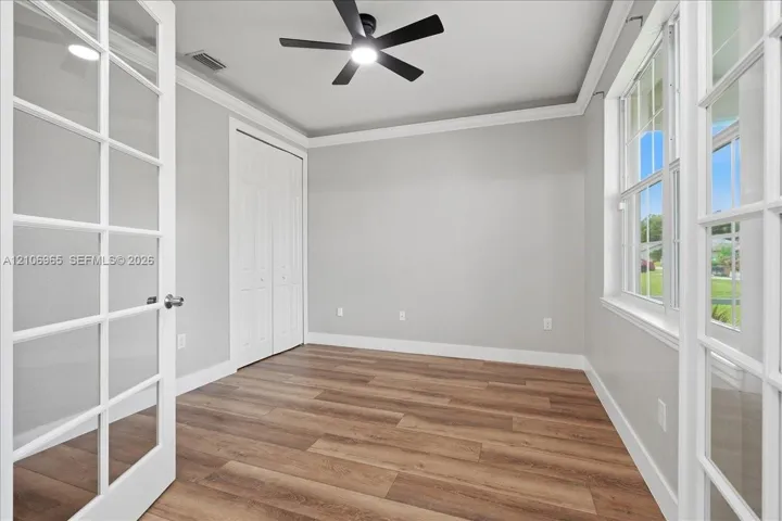 Interior space featuring wood-finish flooring, multi-pane French doors, crown molding, double-door closet, and a ceiling fan with integrated lighting
