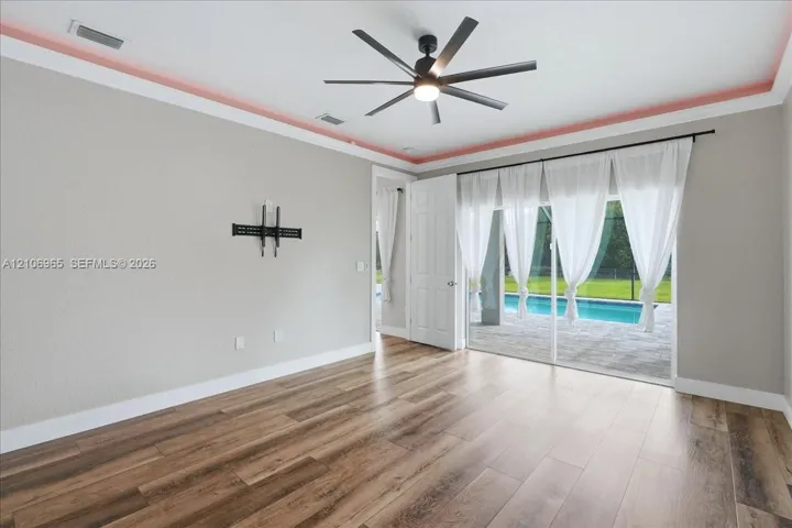 Living area featuring wood-finish flooring, recessed tray ceiling detailing, multi-blade ceiling fan, and sliding glass doors with access to an exterior screened-in pool area