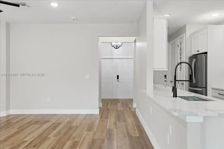 Kitchen featuring a stone-surface breakfast bar, matte black gooseneck faucet, white shaker-style cabinetry, recessed lighting, and wood-finish flooring