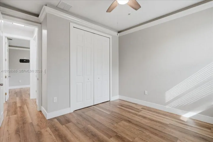 Room featuring wood-finish flooring, crown molding, a ceiling fan with integrated lighting, and a double-panel closet door