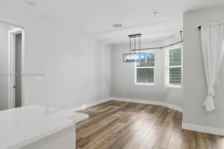 Interior space featuring wood-finish flooring, a contemporary rectangular chandelier, dual windows, and a white countertop with grey veining