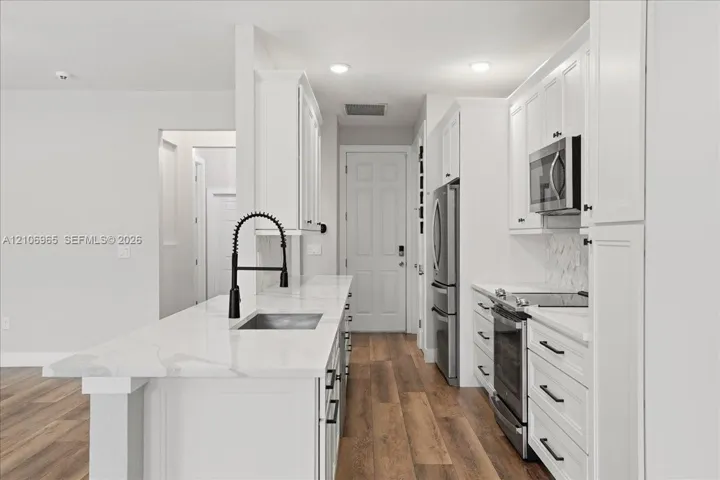 Kitchen featuring white shaker-style cabinetry, white stone-finish countertops, stainless steel appliances, wood-finish flooring, and a matte black gooseneck faucet