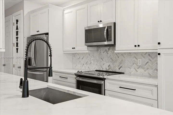 Kitchen featuring white shaker cabinetry, stainless steel appliances, herringbone-pattern stone backsplash, stone countertops, and a matte black gooseneck faucet