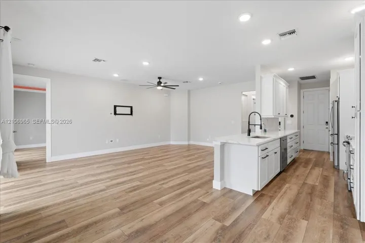 Open concept interior featuring wood-finish flooring, recessed lighting, white cabinetry, solid-surface countertops, and a kitchen island with a matte black faucet