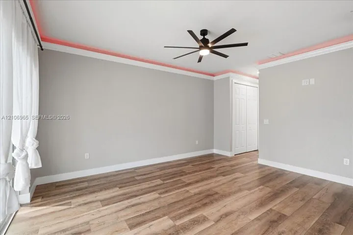 Room featuring wood-finish flooring, multi-blade ceiling fan with integrated lighting, crown molding with accent lighting, and dual-panel interior closet doors