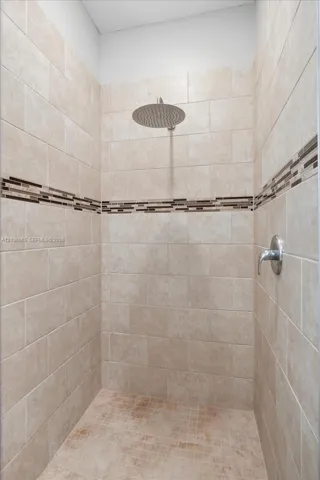 Walk-in shower featuring floor-to-ceiling neutral tile, a decorative glass mosaic accent border, a ceiling-mounted rainfall showerhead, and a wall-mounted chrome control fixture