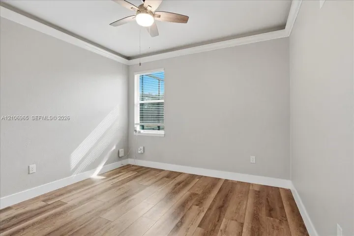 Bright, light-filled bedroom showcasing wood-finish flooring, clean white walls, and a ceiling fan with integrated lighting