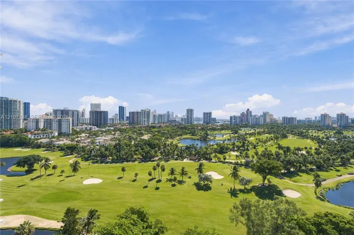 Elevated perspective featuring expansive golf course fairways, scattered mature palms, multiple water hazards, and a panoramic city skyline backdrop