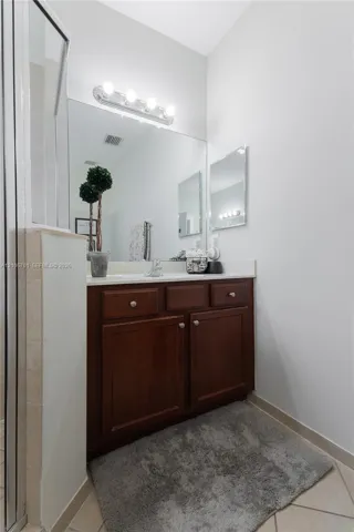 Bathroom vanity with dark wood cabinetry, solid-surface countertop, integrated basin, large wall-mounted mirror, and multi-bulb fixture
