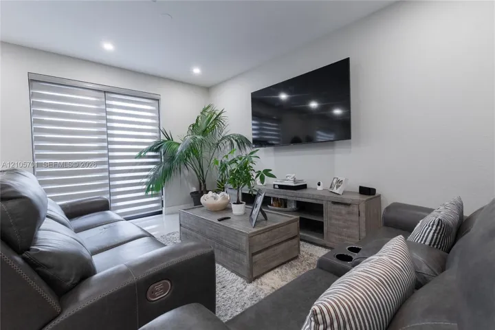 Living space featuring recessed lighting, smooth-finish walls, large-format tile flooring, and sliding glass doors with integrated horizontal window treatments