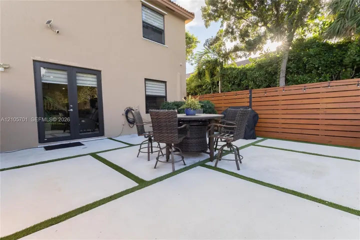 Rear exterior featuring a concrete paver patio with turf inlays, horizontal wood-slat privacy fencing, and double-glass door entry
