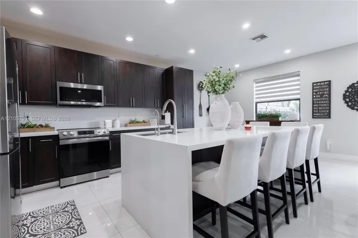 Kitchen featuring dark-finish cabinetry, a central island with a solid-surface countertop, stainless steel appliances, and large-format tile flooring