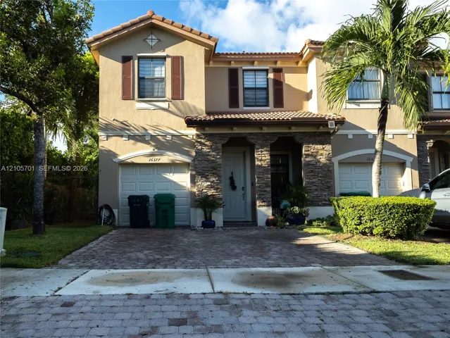 Two-story exterior featuring a stone facade, paver driveway, tile roof, and dark shutter accents
