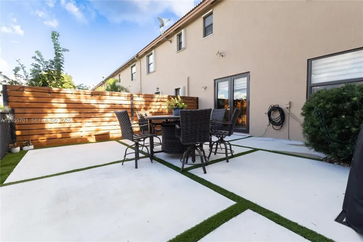 Rear patio featuring large-format concrete pavers with artificial turf inlay and a horizontal wood privacy fence